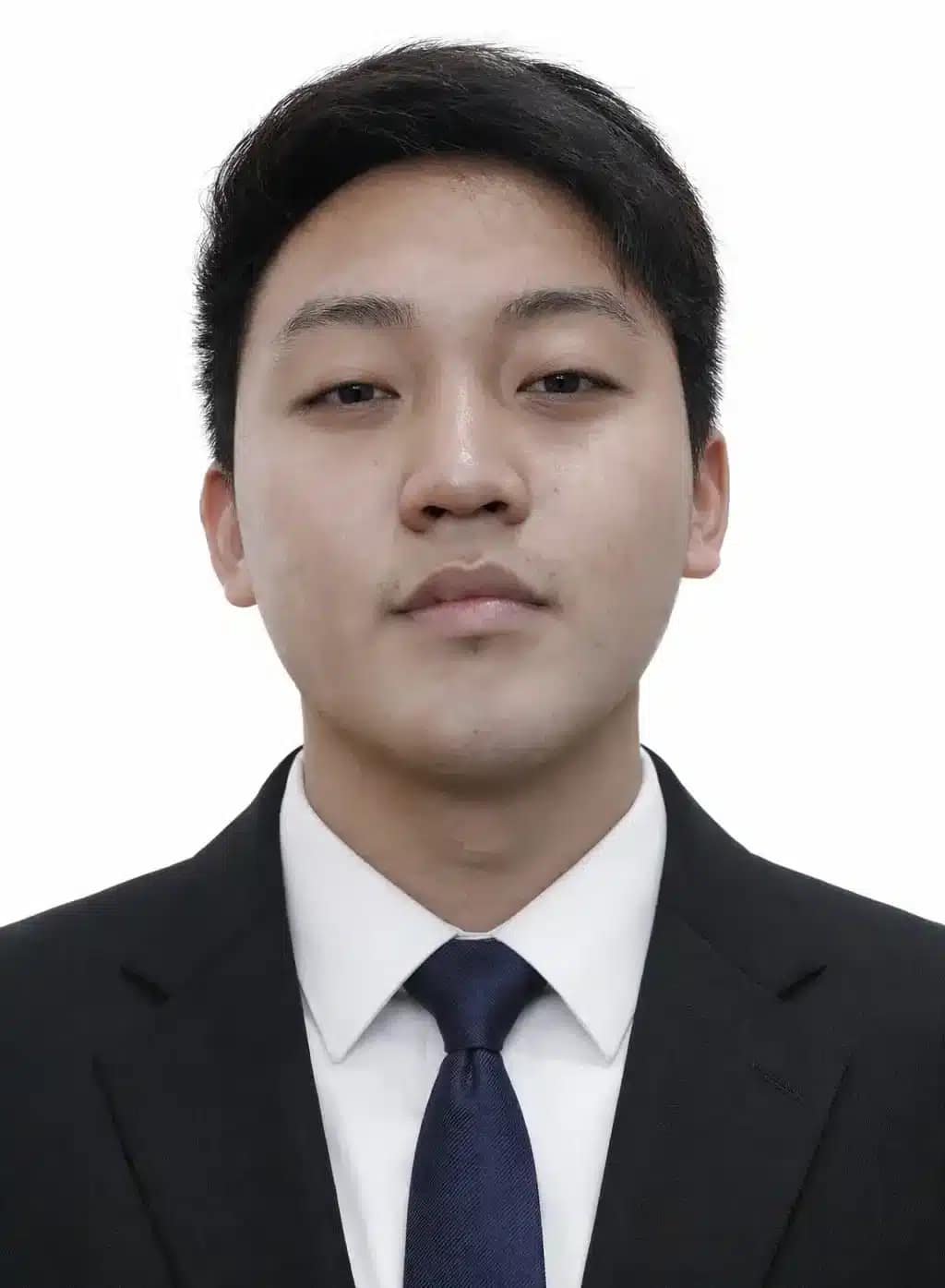 A young man with short black hair, wearing a black suit, white shirt, and dark tie, poses for a formal portrait against a plain white background—perfect for an About page at Better Home Buyer.