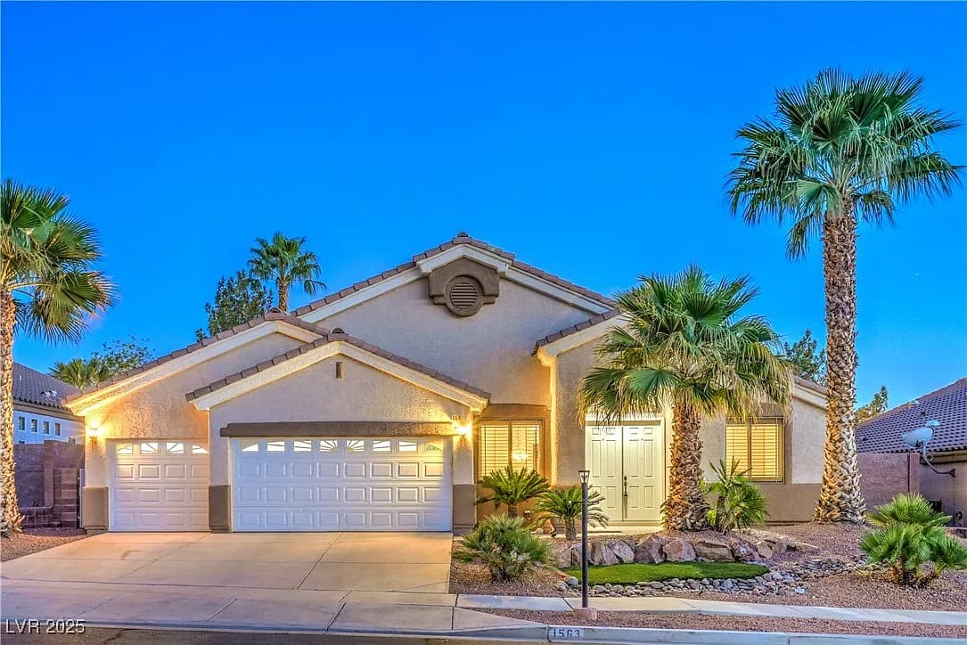 Single-story suburban house with three-car garage, illuminated exterior lights, desert landscaping, and palm trees in the front yard. Perfect opportunity to sell my home as is to a Better Home Buyer. The sky is clear and blue in the early evening.