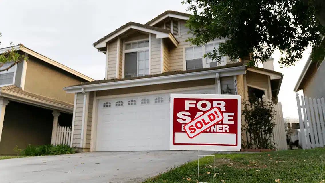 A two-story suburban house with a garage and a For Sale By Owner sign in the yard. A red SOLD! sticker shows the home was sold quickly—perfect for those looking to sell your house fast or find a cash buyer.