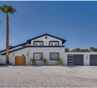 Modern two-story house with white and dark trim, a wooden gate, two-car garage, gravel front yard, and a tall palm tree on the left side.